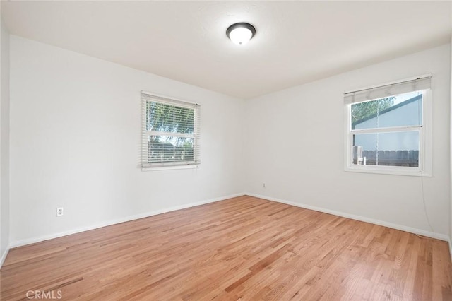 empty room featuring plenty of natural light, light wood-style flooring, and baseboards