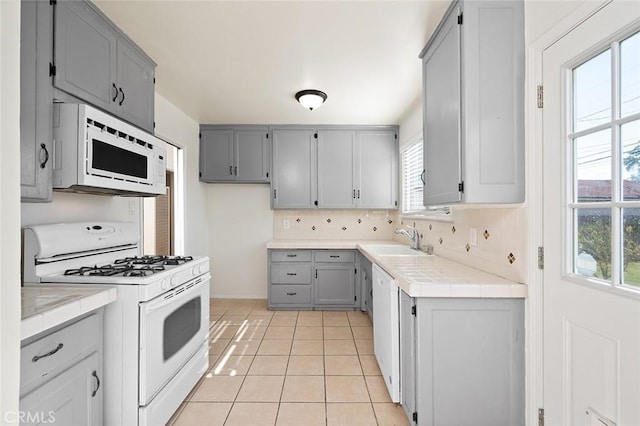kitchen featuring a sink, gray cabinets, plenty of natural light, and white appliances