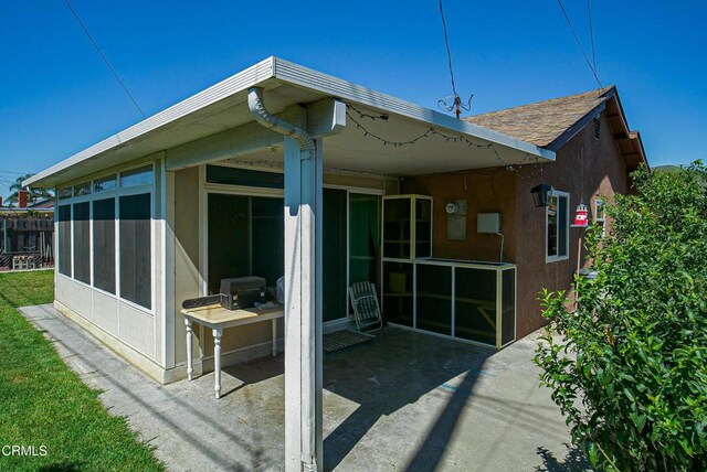 rear view of property with stucco siding, a shingled roof, a patio, and a sunroom