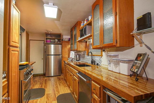 kitchen with brown cabinets, glass insert cabinets, a sink, appliances with stainless steel finishes, and light wood-style floors