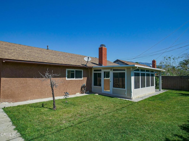 back of property featuring a chimney, stucco siding, a yard, fence, and a sunroom