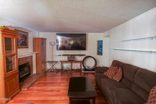 living area featuring a textured ceiling, wood finished floors, and a brick fireplace