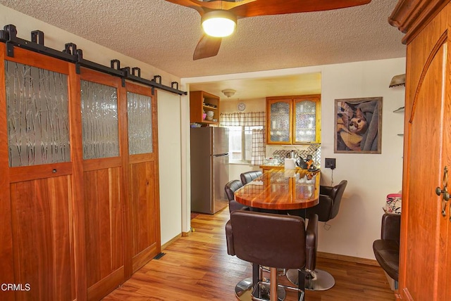 dining area with a textured ceiling, ceiling fan, a barn door, and light wood-style floors