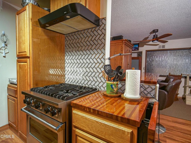 kitchen with butcher block countertops, stainless steel stove, under cabinet range hood, visible vents, and a ceiling fan
