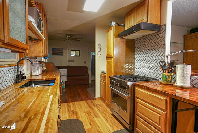 kitchen featuring tasteful backsplash, butcher block counters, under cabinet range hood, a sink, and high end stainless steel range oven
