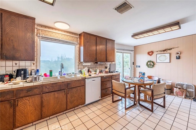 kitchen with tile counters, white dishwasher, a sink, backsplash, and visible vents