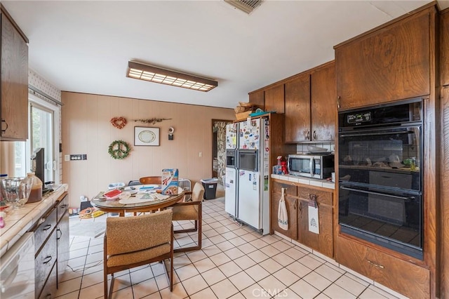 kitchen with visible vents, tile countertops, stainless steel microwave, dobule oven black, and white refrigerator with ice dispenser