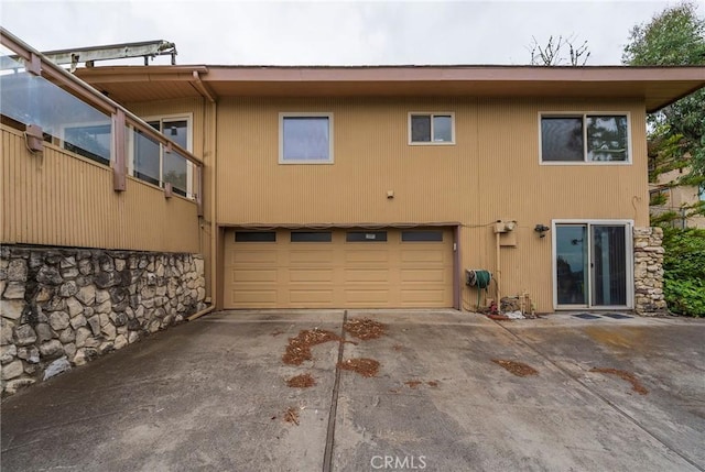 back of property featuring concrete driveway, an attached garage, and stone siding