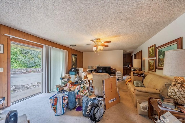 carpeted living area with a textured ceiling, wood walls, ceiling fan, and visible vents