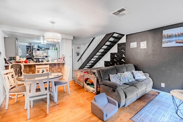 living area with visible vents, light wood-style flooring, and stairway