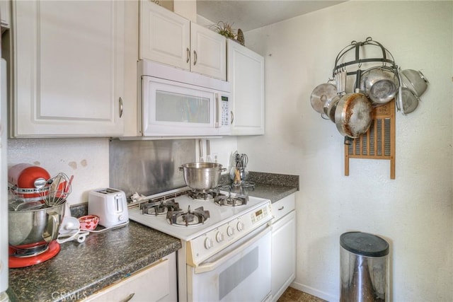 kitchen featuring white cabinets, dark countertops, and white appliances