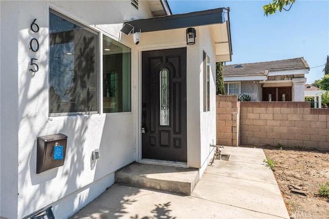 view of exterior entry with stucco siding and fence