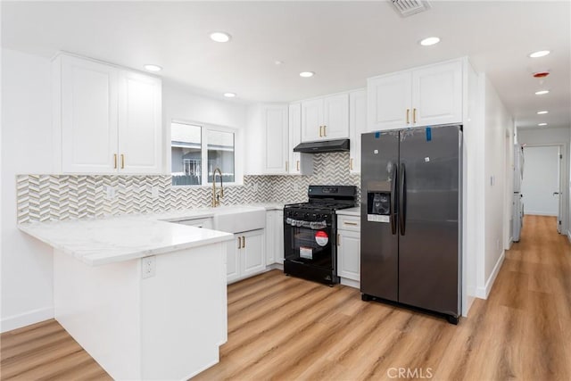 kitchen with black appliances, under cabinet range hood, a peninsula, white cabinets, and a sink
