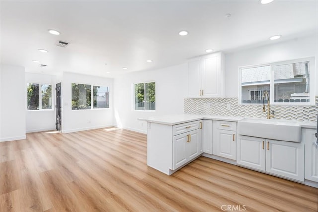 kitchen featuring a peninsula, a sink, backsplash, white cabinets, and recessed lighting