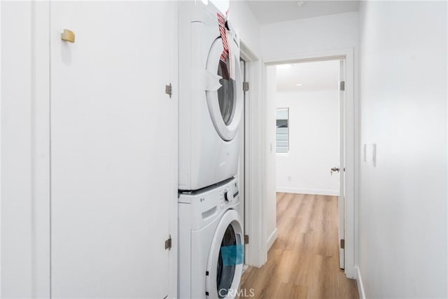 washroom featuring stacked washer and clothes dryer, light wood finished floors, and baseboards