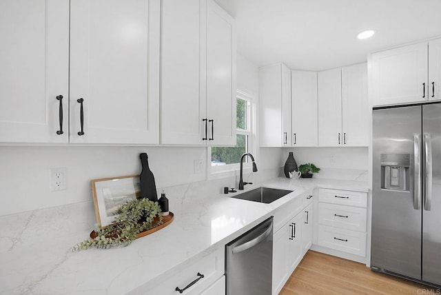 kitchen featuring light stone counters, white cabinets, stainless steel appliances, and a sink