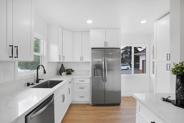 kitchen featuring stainless steel appliances, a sink, white cabinetry, light wood-style floors, and light stone counters