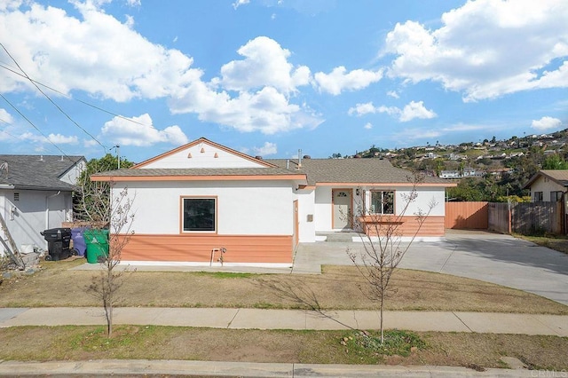 view of front of home with stucco siding, driveway, fence, and roof with shingles