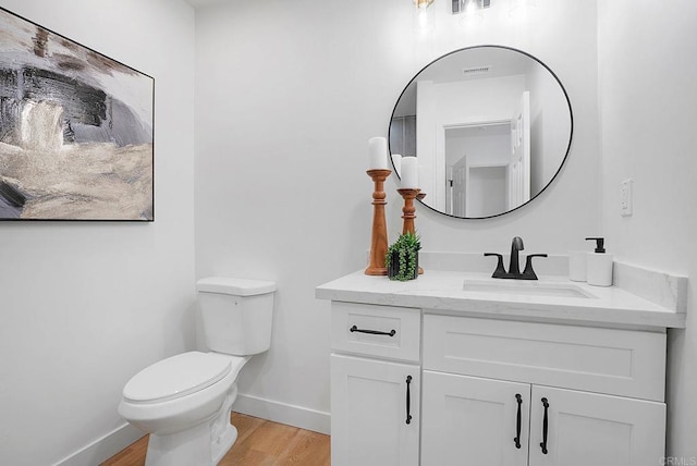 half bathroom featuring baseboards, toilet, vanity, and wood finished floors