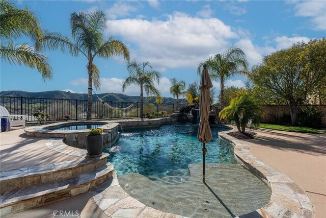 view of swimming pool featuring a fenced backyard, a mountain view, and a pool with connected hot tub