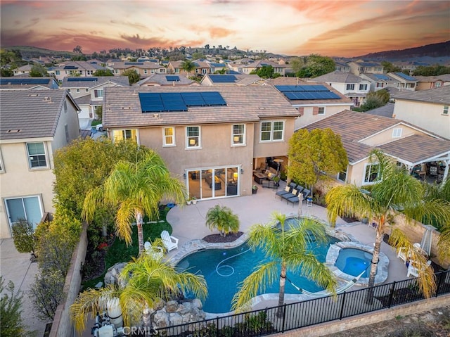 back of property with a fenced backyard, an in ground hot tub, a residential view, and stucco siding