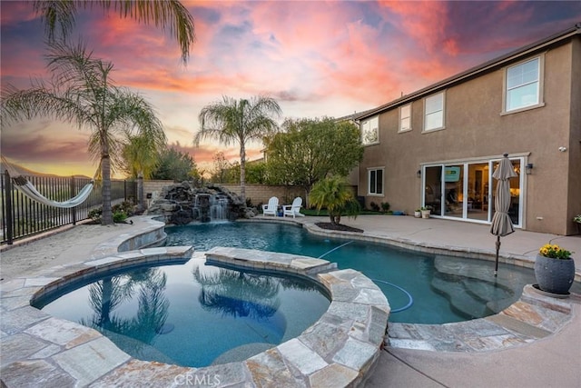 pool at dusk featuring a patio area, a pool with connected hot tub, and a fenced backyard