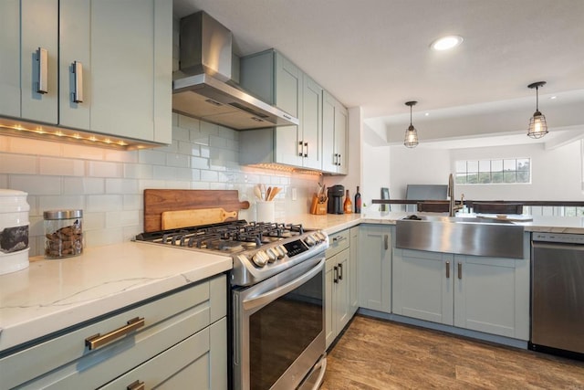 kitchen featuring stainless steel appliances, a sink, dark wood-style flooring, decorative backsplash, and wall chimney range hood