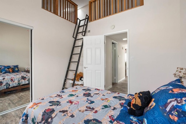 bedroom with a closet, wood finished floors, a high ceiling, and baseboards