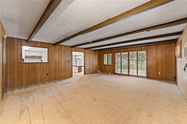 empty room with beam ceiling, a textured ceiling, carpet, a notable chandelier, and wood walls