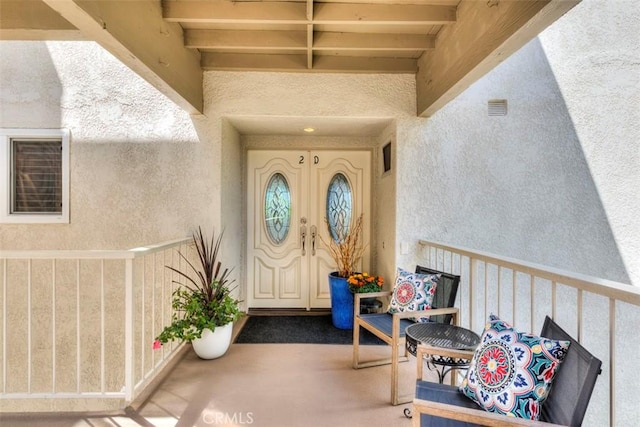 view of exterior entry with a balcony, visible vents, and stucco siding