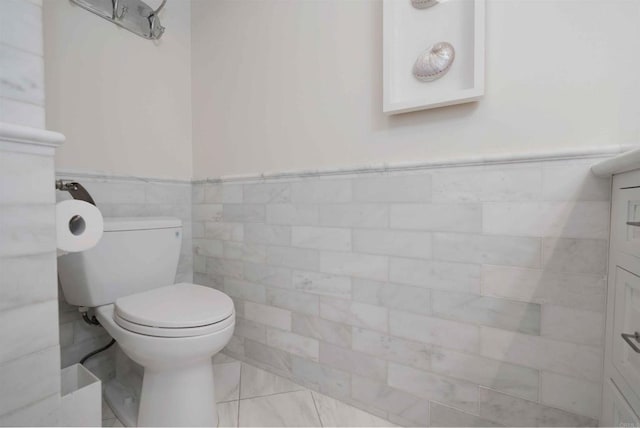 half bathroom with tile walls, a wainscoted wall, and toilet