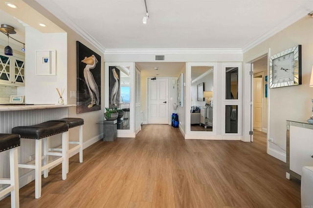 entryway with baseboards, crown molding, wood finished floors, and visible vents