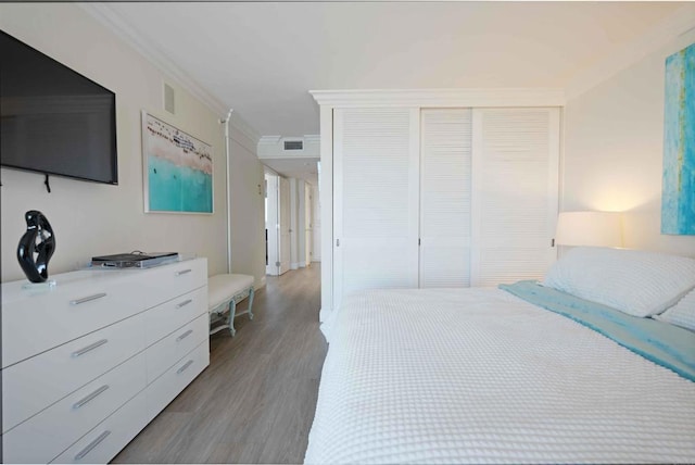bedroom with wood finished floors, a closet, crown molding, and visible vents