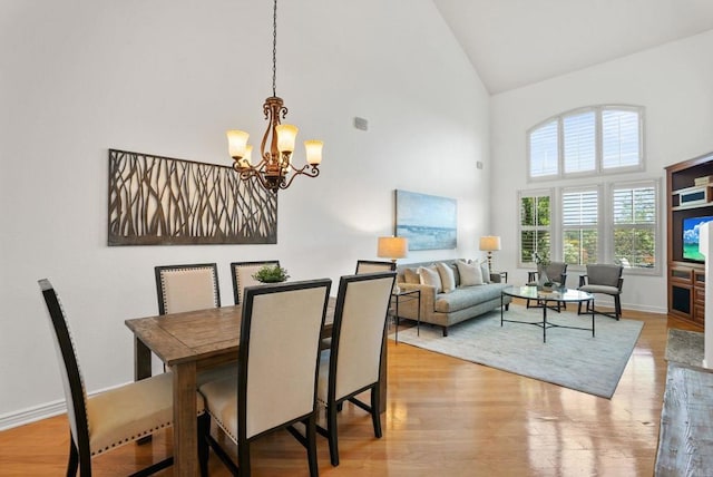dining space featuring high vaulted ceiling, a chandelier, light wood-style floors, and baseboards