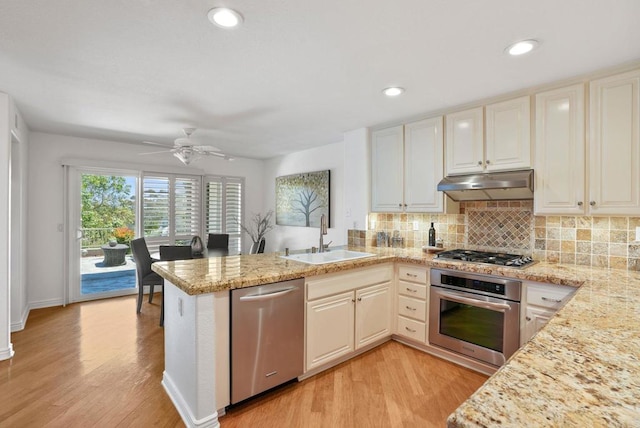 kitchen with stainless steel appliances, a sink, under cabinet range hood, a peninsula, and light wood-type flooring