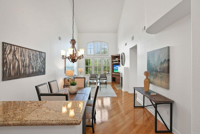 dining room featuring a towering ceiling, light wood-type flooring, a chandelier, and baseboards