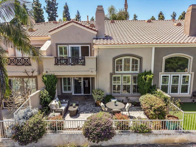 back of house with a chimney, a balcony, stucco siding, a tiled roof, and a patio