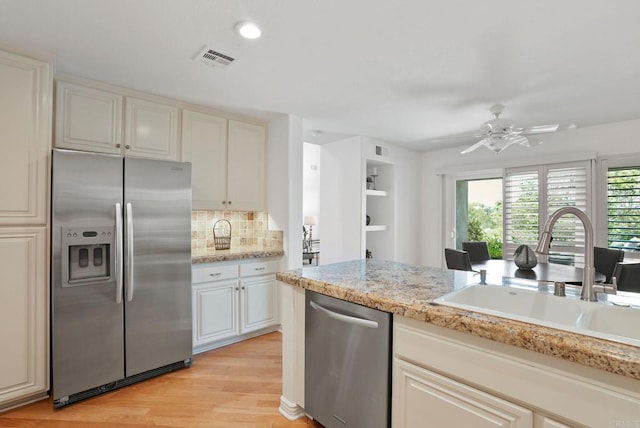 kitchen featuring stainless steel appliances, a sink, light wood-style flooring, decorative backsplash, and ceiling fan