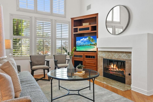 living area featuring a tile fireplace, wood finished floors, a towering ceiling, and baseboards
