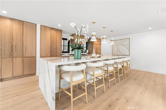 kitchen featuring visible vents, a large island with sink, a breakfast bar, and light wood-type flooring