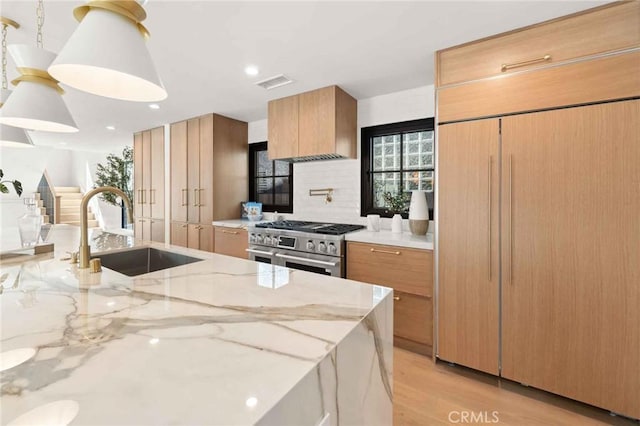 kitchen featuring light stone counters, a sink, range with two ovens, decorative backsplash, and visible vents