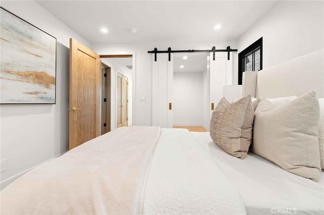 bedroom with recessed lighting, a barn door, and wood finished floors