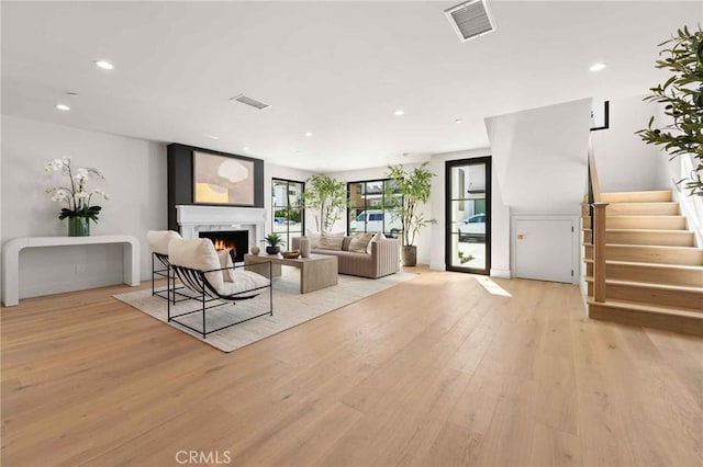 living room featuring a warm lit fireplace, visible vents, and light wood finished floors