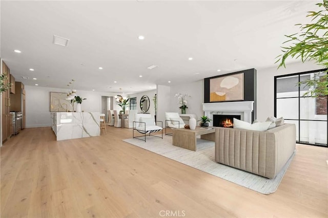 living area with light wood-style floors, recessed lighting, and a warm lit fireplace