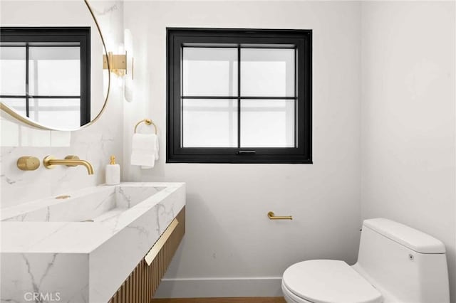 half bathroom with toilet, baseboards, a healthy amount of sunlight, and vanity