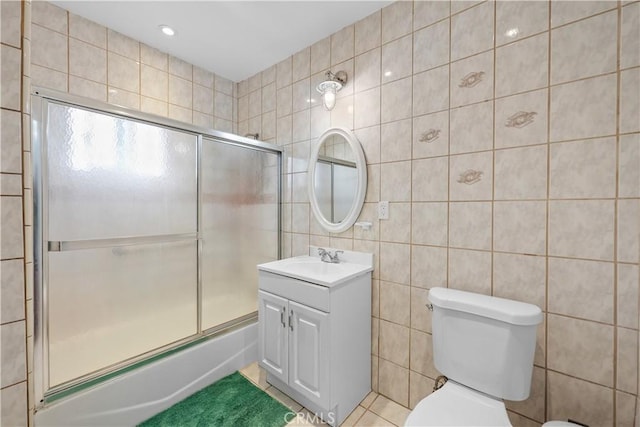 bathroom featuring tile patterned flooring, tile walls, shower / bath combination with glass door, toilet, and vanity