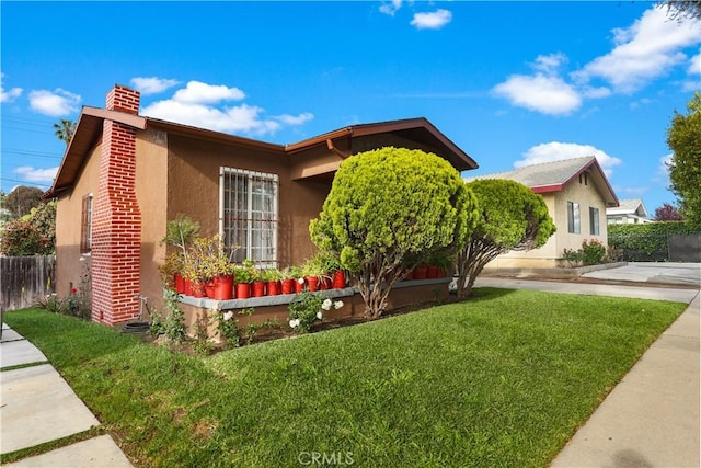 ranch-style house featuring stucco siding, fence, a chimney, and a front lawn