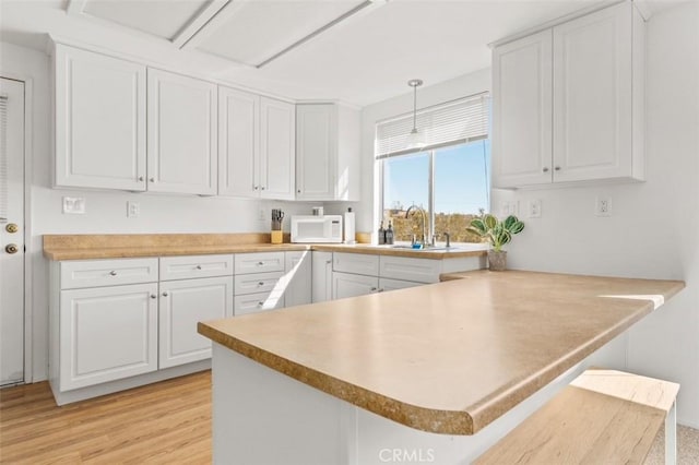 kitchen with white cabinets, a peninsula, a sink, and white microwave