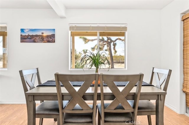 dining area featuring light wood-style flooring, baseboards, and beam ceiling