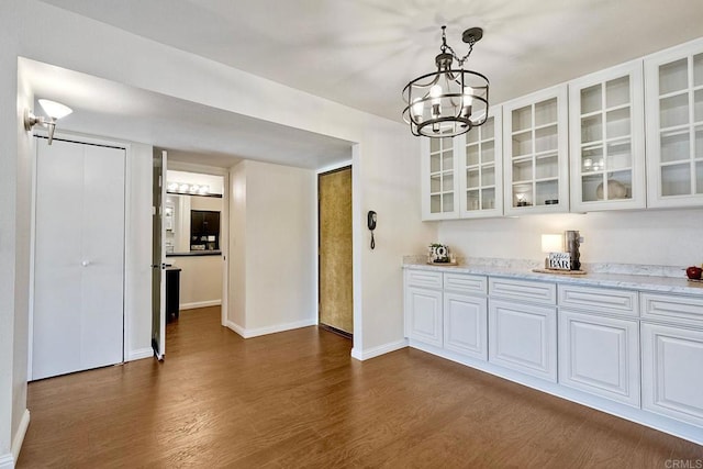 unfurnished dining area with dark wood finished floors, baseboards, and a chandelier